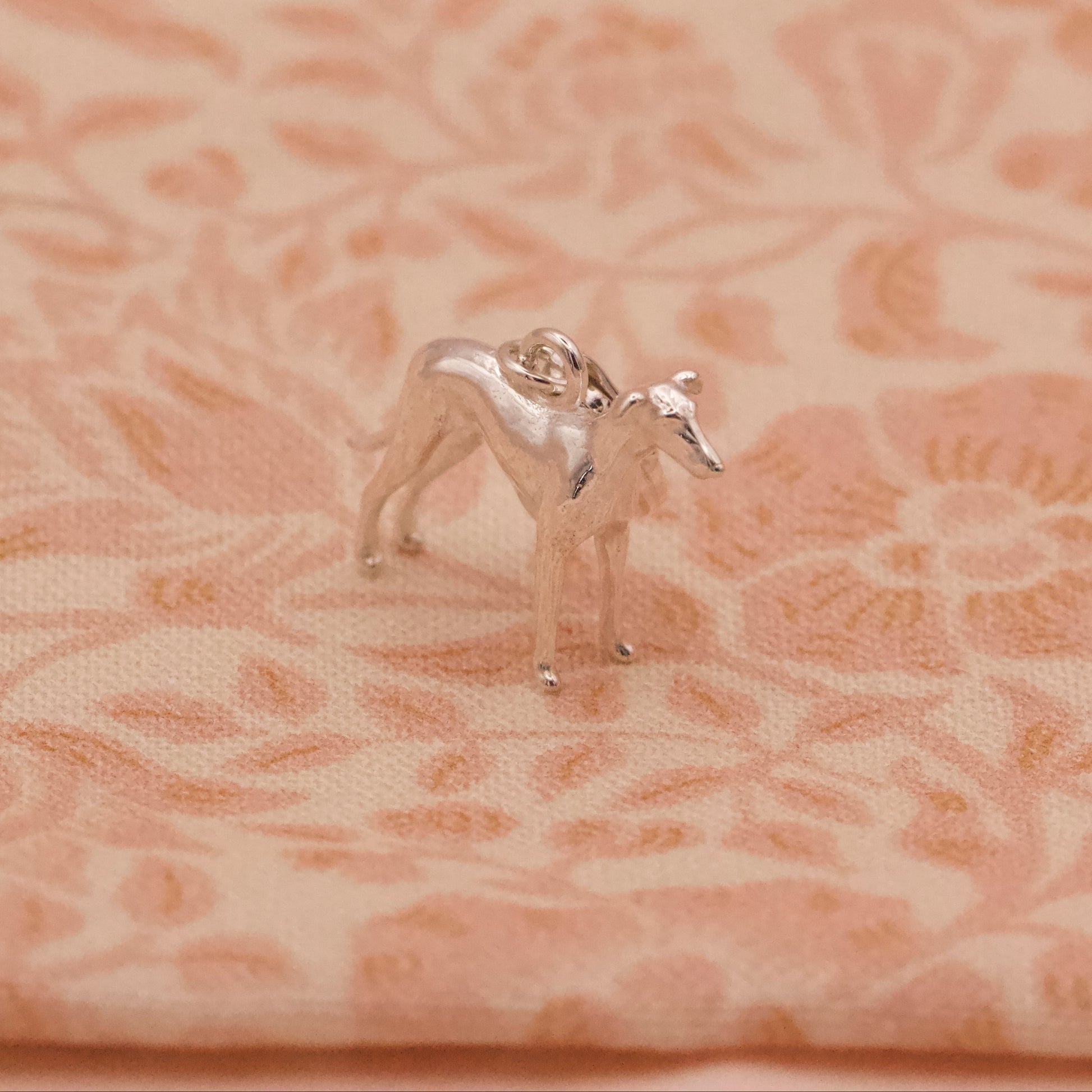 Small silver whippet dog figurine on a pink floral fabric background